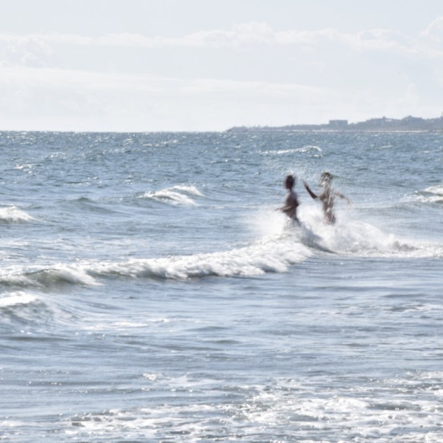 People running into the waves at the beach in Chioggia, Italy with the coast in the distance.