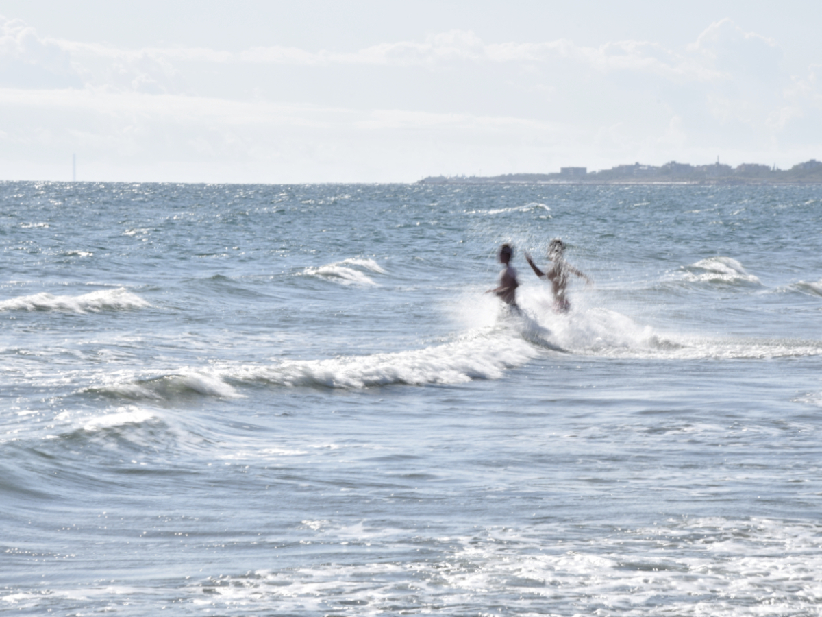 People running into the waves at the beach in Chioggia, Italy with the coast in the distance.