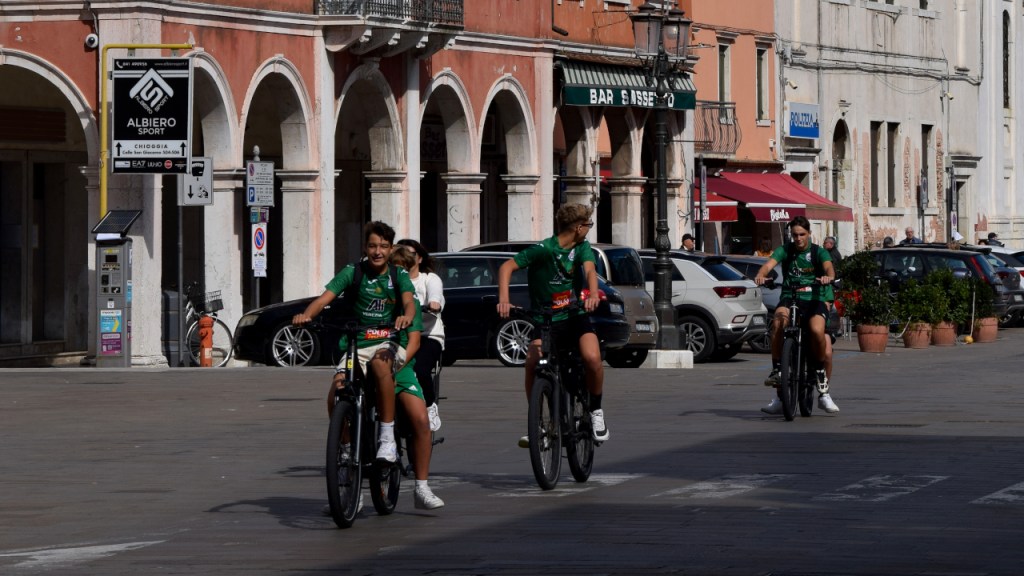Kids in green shirts riding bikes on the middle street of Chioggia, Italy.
